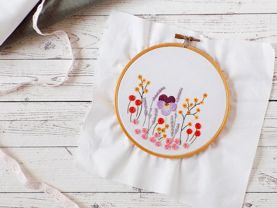 Embroidered flowers on white fabric on a hoop, with embroidery thread and scissors scattered around